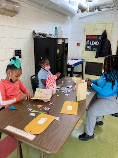 Girls sit at table with art supplies creating greeting cards