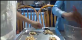 screengrab of one person mixing while another places cookies on a cookie tray