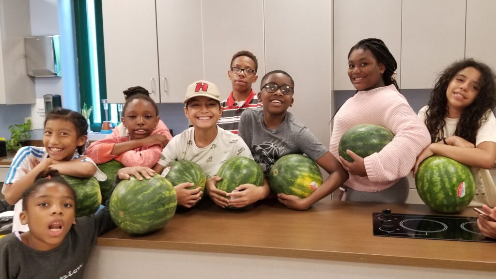 A group of young people pose in a kitchen each holding a watermelon