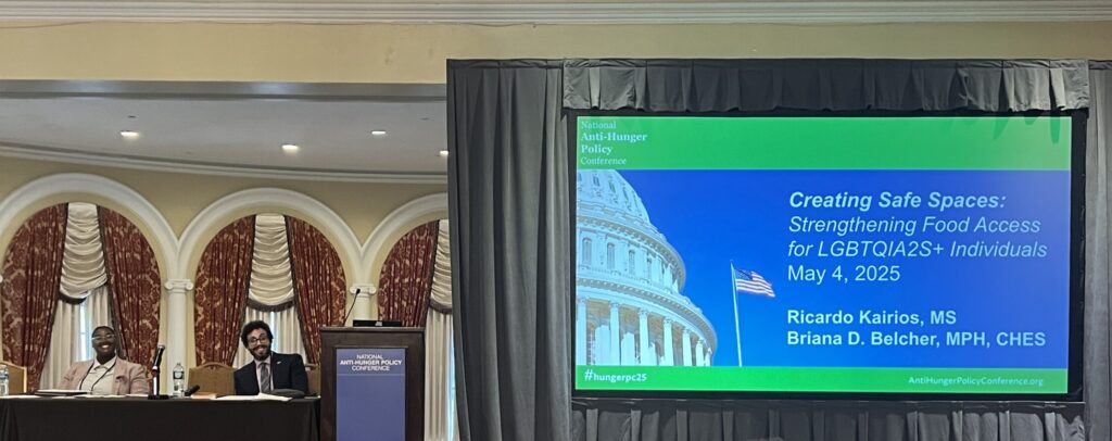 Picture of a large screen with the words National Anti-Hunger Policy Conference to the left are a man and a woman behind a long table.