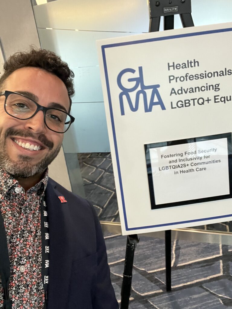 A picture of  Ricardo Kairios in front of a sign that reads GLMA Health Professionals Advancing LGBTQ+ Equality