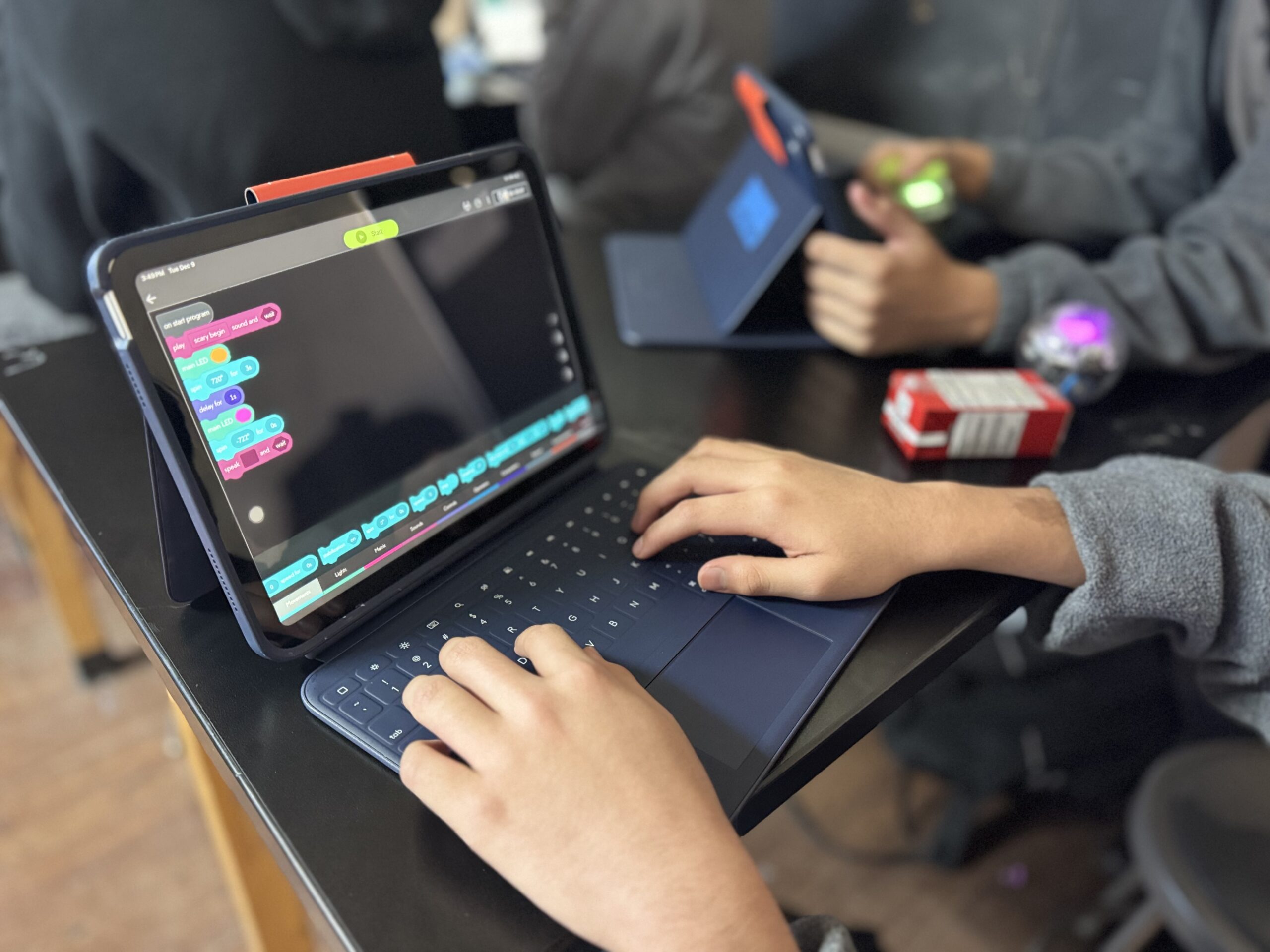 A an open laptop showing blue, aqua and red blocks on the screen. With a young persons hands typing on the keyboard.