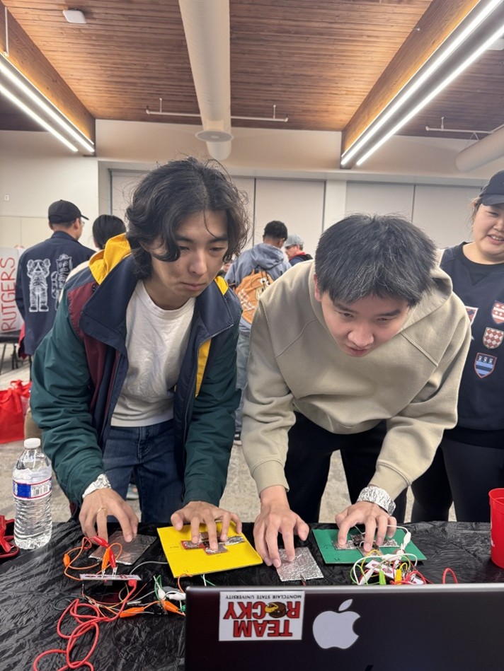 Two young men concentrate on a screen while pressing buttons on colorful pads