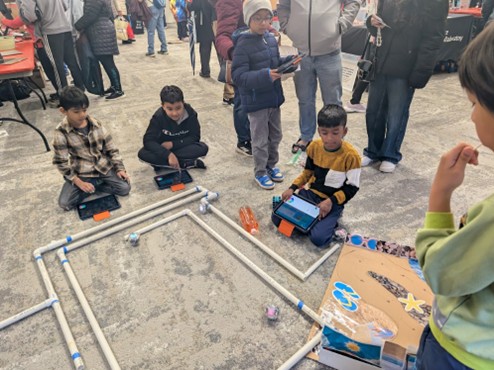 Young children sit on the floor with a computer, guiding SPIRO robots