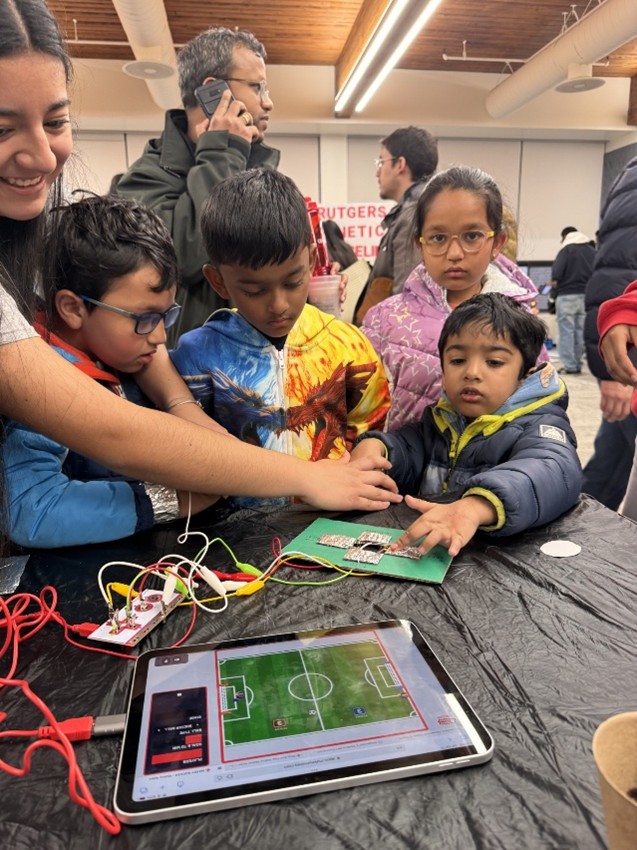 4 young people gather around an iPad playing a game while a teenager looks on and encourages them